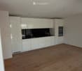 Empty kitchen with white cabinets, black countertop, and wooden flooring. No furniture or appliances are present.