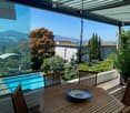Balcony with wooden table and chairs, overlooking a swimming pool and scenic mountain view.