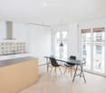 Modern kitchen with white cabinets, wooden island, black dining table, and pendant light. Features a balcony view through large windows.