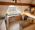 Bright, airy kitchen with wooden cabinets, granite countertops, and modern appliances. Features a large window with a view, built-in lighting, and potted plants on the counters.