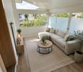 Bright living room with wooden flooring, large windows, a sectional sofa, coffee table, side table, and potted plants.