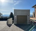 Modern concrete building with a large garage door, surrounded by a paved area with a view of the city and mountains in the background.