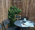 Outdoor seating area with a round black metal table, two wicker chairs, a cup, and a sign that reads "Lieblingsplatz" in German.