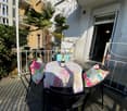 Balcony with a round table, chairs, and decorative cushions, overlooking a palm-lined street.