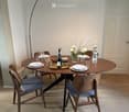 A modern dining area with a round wooden table, four chairs, a floor lamp, and a vase with flowers on the table.