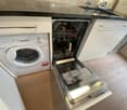 Modern kitchen with a white cabinetry, a stainless steel dishwasher, and a white washing machine. The floor is wooden, and the countertop is black.