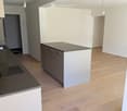 Modern kitchen with light wooden flooring, white and grey cabinets, and a black countertop island.