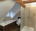 Modern bathroom with a bathtub, toilet, and walk-in shower, featuring exposed wooden beams and a skylight window.