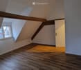 Empty attic room with wooden flooring, exposed wooden beams, and a skylight window. No furniture or equipment present.