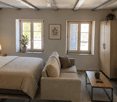 A modern, well-lit bedroom with a large bed, sofa, coffee table, nightstand, lamp, cabinet, television, picture frames, and plants.