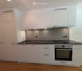 Modern kitchen with white cabinets, stainless steel sink, and built-in oven. Features sleek countertops and integrated lighting.