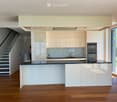 Modern kitchen with white cabinets, a central island, and stainless steel appliances. The space features wooden flooring and a staircase leading to an upper level.