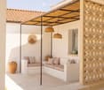 Outdoor patio with a white built-in sofa, decorative vases, and a decorative wall piece. The area is covered by a pergola with hanging wicker lamps.