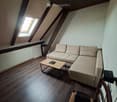 Attic living room with wooden floors, slanted wooden ceiling, skylight window, sofa, coffee table, and a wicker chair.