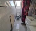 Small bathroom with tiled walls and floor, toilet, sink, and a shower area with a floral curtain. A radiator is mounted on the wall.
