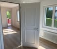Empty room with wooden flooring, white walls, and a large window with a view of greenery. Radiators are visible on both sides of the room.