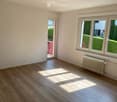 Empty room with wooden flooring, white walls, large windows, and a radiator. A sliding door leads to an outdoor area.