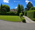 Well-maintained garden with a neatly trimmed lawn, a gravel pathway, and trimmed hedges leading to a house with a tiled roof.