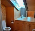 Cozy attic bathroom with wooden walls and ceiling, featuring a toilet, double sink with wooden cabinet, and a skylight window above the sink.