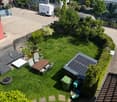 Garden / Outdoor Area. A well-maintained garden with a wooden table, chairs, lounge seating, a solar panel structure, and a small water feature. The area is surrounded by greenery and includes a trash bin and a small shed.