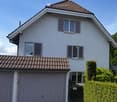 House. Two-story house with white exterior, brown tiled roof, multiple windows with shutters, and a garage.