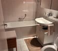 Modern bathroom with a bathtub, sink, toilet, and shower. Features marble flooring, tiled walls, and a towel on a wooden stool.