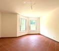 Empty room with beige walls, red tiled floor, and two windows with white frames. No furniture or equipment present.