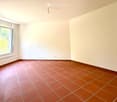 Empty room with tiled floor and white walls, featuring two large windows with open shutters allowing natural light.