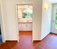 Hallway with terracotta tiles, leading to a kitchen and bathroom. Features a white door with glass panel and a wall-mounted light fixture.