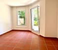 Empty room with tiled floor and white walls, featuring a large window and a sliding glass door leading outside.