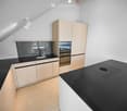 Modern kitchen with light-colored cabinets, black countertops, a built-in oven, and a sink with a modern faucet.