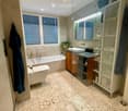 Modern bathroom with a bathtub, toilet, sink, and large mirror. Features wooden cabinetry, patterned tiles, and a glass-enclosed shower area.
