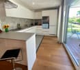Modern kitchen with white cabinets, wooden flooring, island with bar stool, sink, oven, and decorative vase on counter.