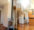 Modern interior with a wooden staircase, a central fireplace, and a kitchen area featuring cabinets and an island.