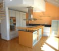 Modern kitchen with white cabinets, a central island, built-in appliances, and a spiral staircase leading to an upper level.
