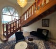 Elegant living room with a staircase, chandelier, patterned rug, sofa, chairs, and tables.