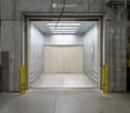 Industrial-style garage with a large open space, concrete floors and walls, a large garage door, and a ladder leading to an upper level.