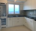 Modern kitchen with white cabinets, dark countertops, and stainless steel appliances. Features a large window with a view of rooftops.