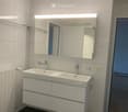 Modern bathroom with white tiles, double sink, mirrored cabinet, and sleek fixtures.