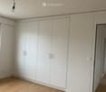 Empty room with light wooden flooring and white built-in wardrobes, featuring a single ceiling light fixture.