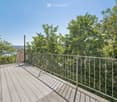 Wooden deck with metal railing, surrounded by lush green trees and a clear blue sky, offering a scenic view of the landscape.