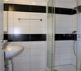 Modern bathroom with white and black tiled walls, a white sink, and a glass-enclosed shower stall.