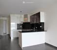 Modern kitchen with white cabinets, black countertops, stainless steel sink, and range hood. Features include pendant lighting and a dark tiled floor.