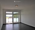 Empty room with dark tiled floor, white walls, and large sliding glass door leading to a balcony with outdoor view.