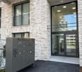 Modern building entrance with glass doors, mailboxes, and a balcony visible above.