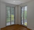 Empty room with light wooden flooring, white walls, and large windows with blinds. No furniture or equipment present.