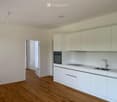 Modern kitchen with white cabinets, a stainless steel sink, and an oven, featuring light wooden flooring and white walls.