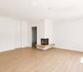 Empty room with light wooden flooring, white walls, and a built-in fireplace with a stone surround.