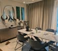 Modern dining area with a white marble table, black chairs, a large mirror, a cabinet with a skull decor, and potted plants.