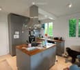 Modern kitchen with grey cabinets, wooden island, stainless steel appliances, and a dog in the corner.